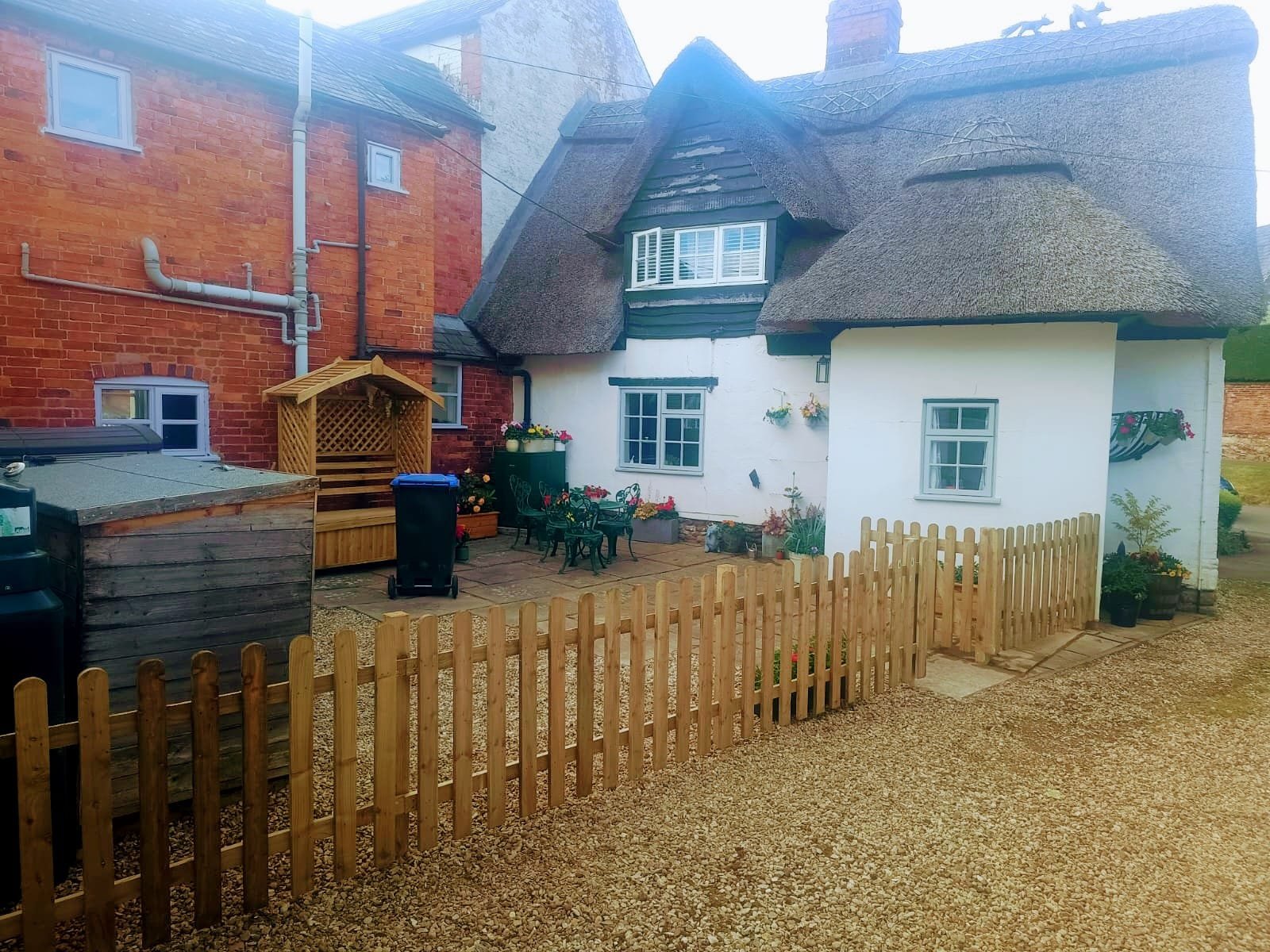 Traditional picket fence enclosing garden of cottage with thatched roof
